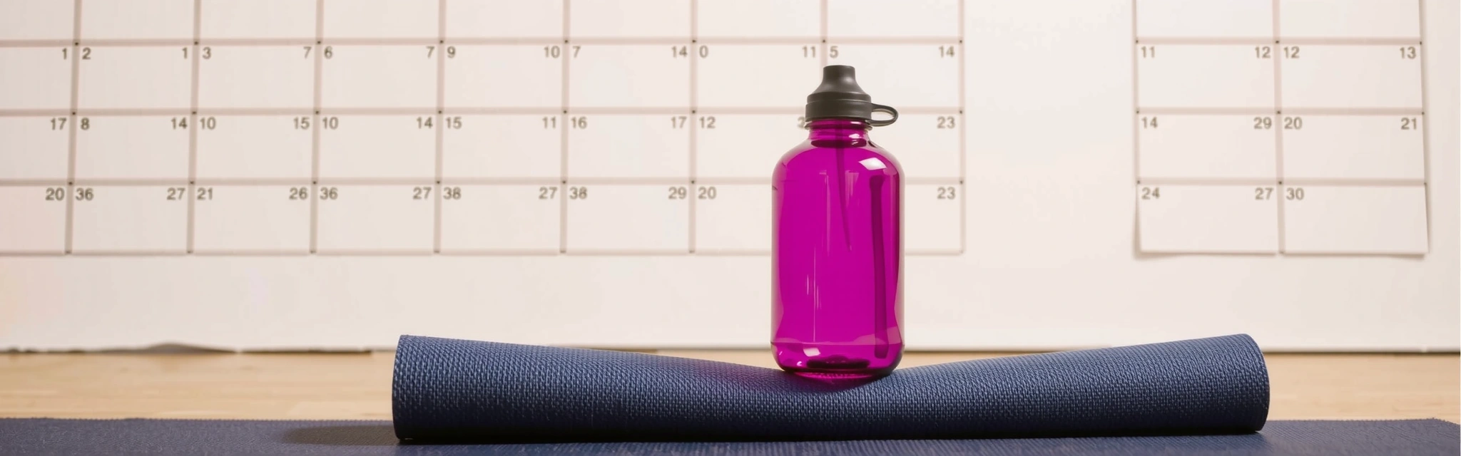 A serene yoga mat and water bottle in front of a blurred calendar, symbolizing a peaceful and organized schedule